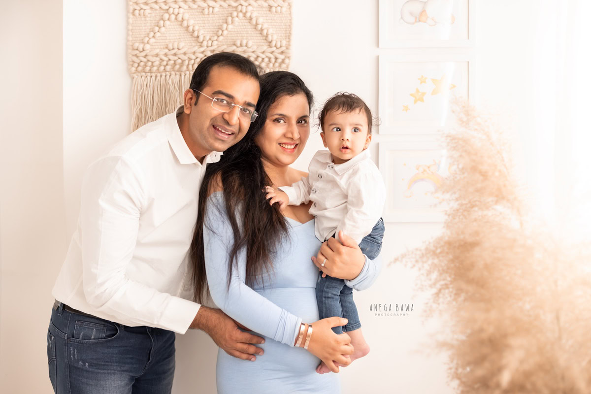 1-year-old boy posing with mom and dad against a backdrop of bushes and beige scenery, captured by Anega Bawa Family Photographer Gurgaon (Delhi NCR).