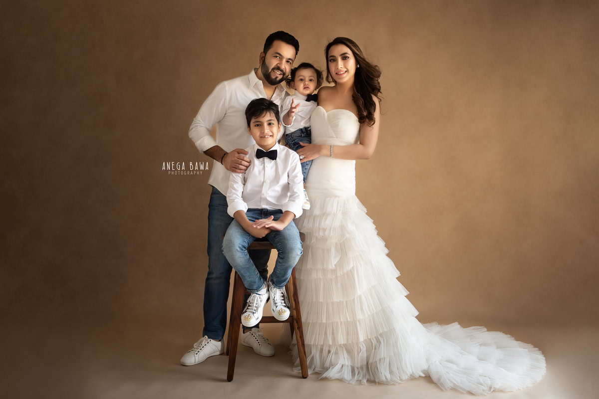 1-year-old boy posing with mom, dad, and elder brother against a warm brown backdrop. Captured by Anega Bawa Photography, Gurgaon (Delhi NCR).