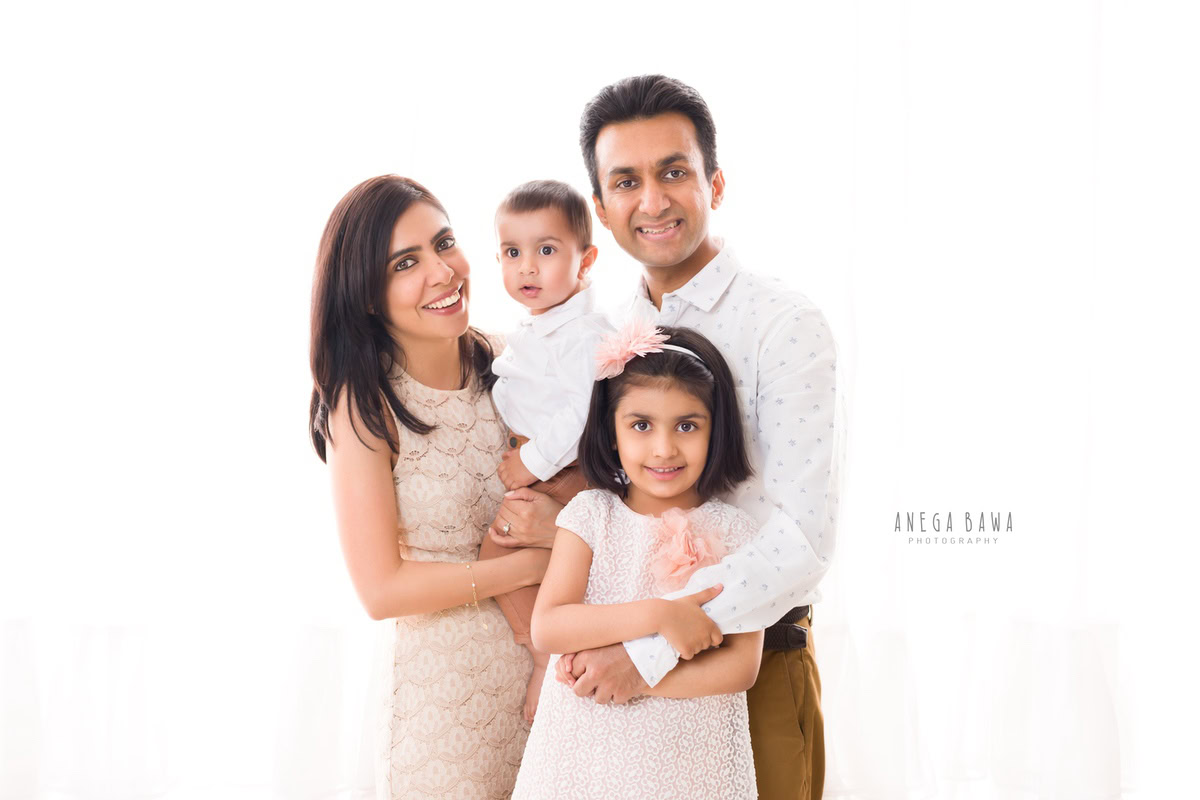 1-year-boy posing with mom, dad, and elder sister against a serene white backdrop, beautifully captured by Anega Bawa Photography for a family photoshoot in Gurgaon (Delhi NCR).