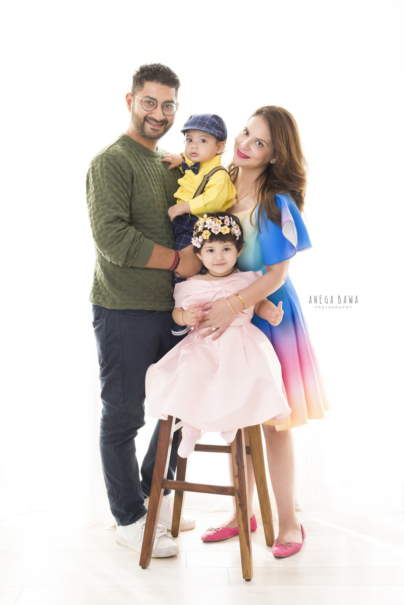 1-year-old boy posing with mom, dad, and elder sister against a white backdrop, captured by Anega Bawa Family Photographer Gurgaon (Delhi NCR).