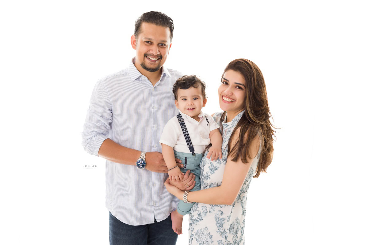 1-year-old boy confidently posing with his mom and dad against a clean white backdrop. Professionally captured by Anega Bawa Photography, Gurgaon (Delhi NCR).