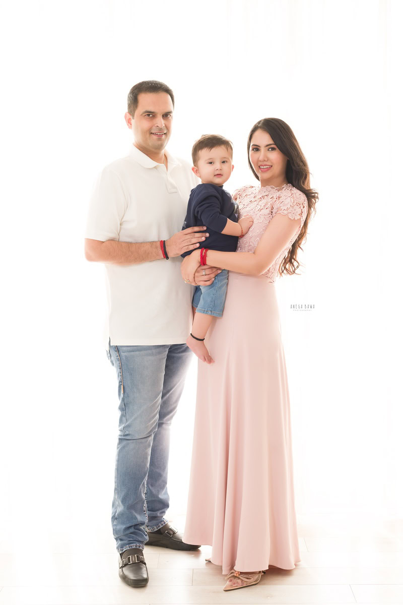 1-year-old boy posing with mom and dad in a charming family photoshoot against a white backdrop, captured by Anega Bawa, renowned family photographer in Gurgaon (Delhi NCR).