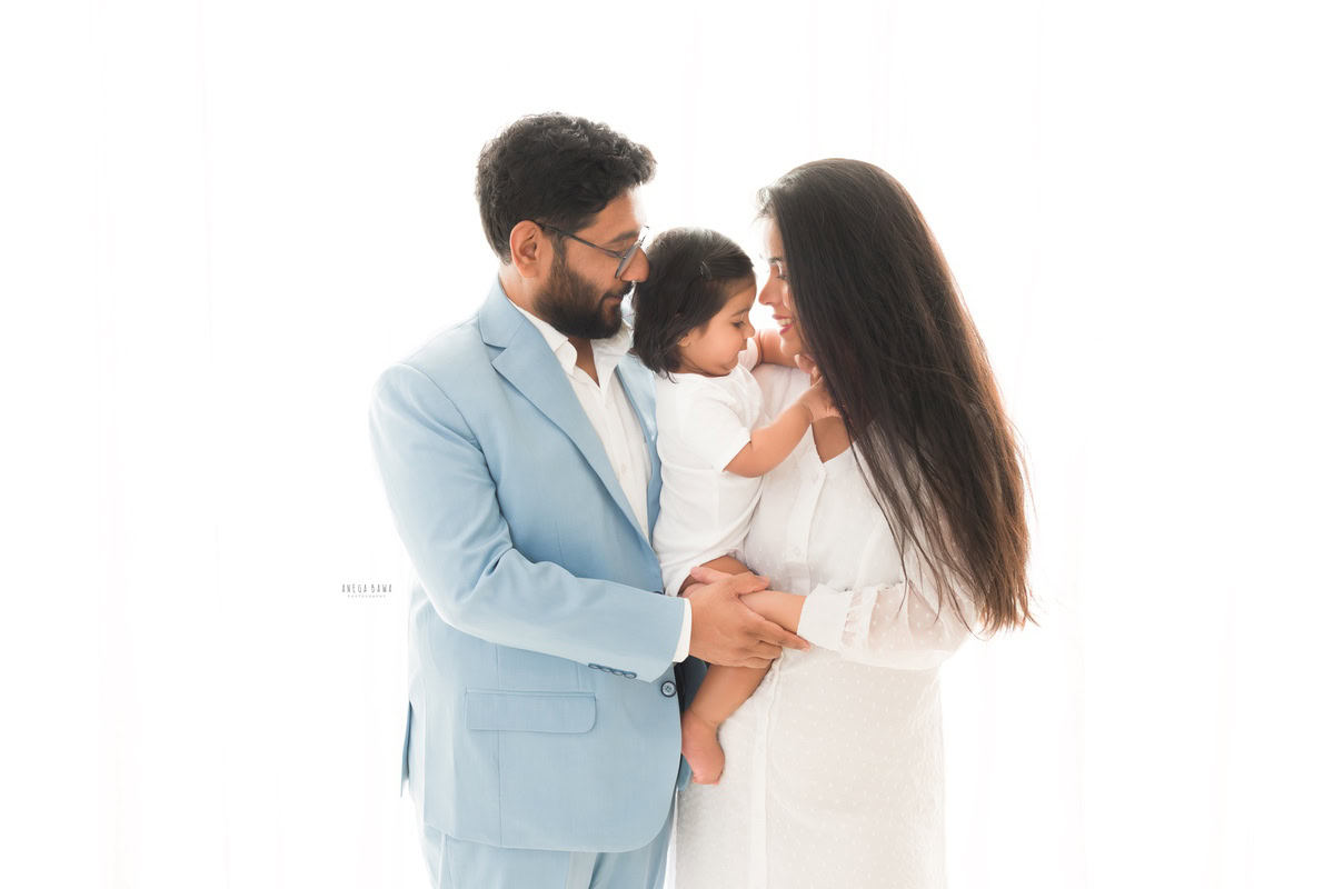 1-year-boy posing with mom and dad against a white backdrop, beautifully captured by Anega Bawa Photography for a family photoshoot in Gurgaon (Delhi NCR).