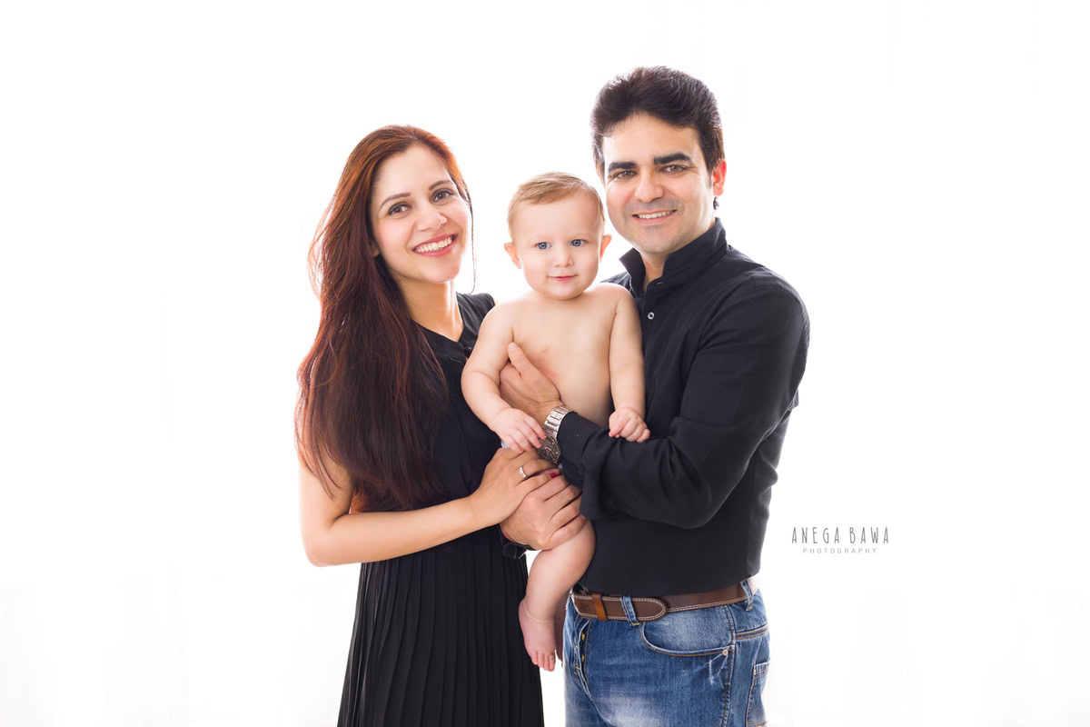1-year-boy posing with mom and dad against a serene white backdrop, captured by Anega Bawa Photography for a family photoshoot in Gurgaon (Delhi NCR).