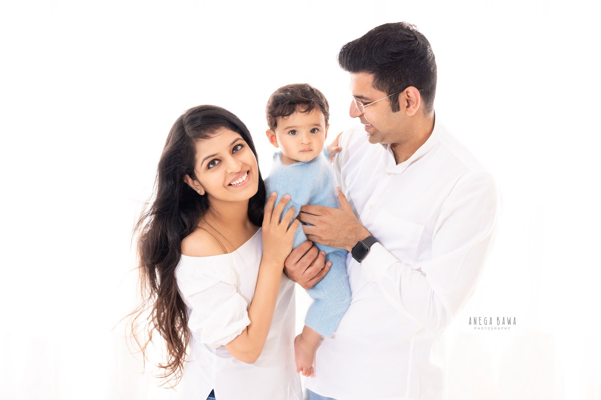 1-year boy posing with mom and dad against a white backdrop, captured by Anega Bawa Photography for a family photoshoot in Gurgaon (Delhi NCR).