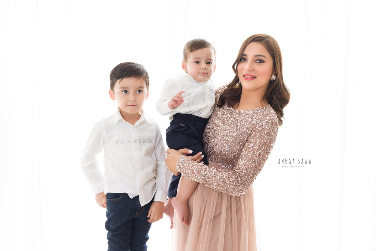 1-year-old boy posing with mom and elder brother against a white backdrop, captured by Anega Bawa Family Photographer Gurgaon (Delhi NCR).