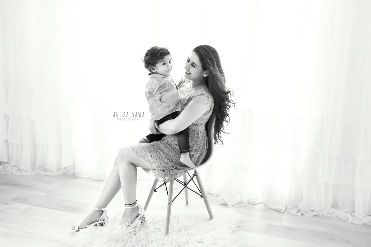 1-year-old boy posing with mom while seated on a chair against a white backdrop, captured by Anega Bawa Family Photographer Gurgaon (Delhi NCR).