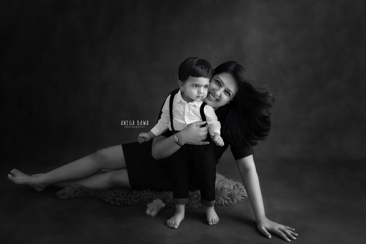 1-year-old boy posing with mom seated on a floor with a beige rug against a black backdrop, captured by Anega Bawa Family Photographer Gurgaon (Delhi NCR).