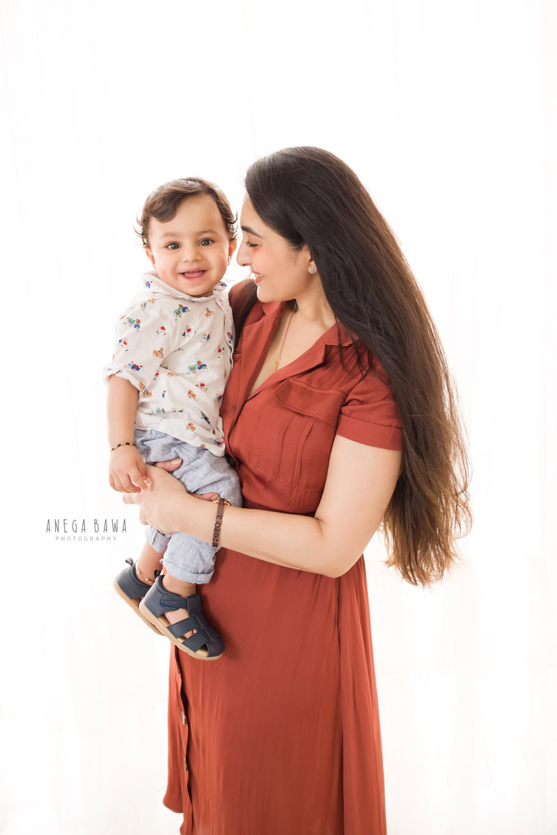Sure: 1-year-old boy posing with mom against a white backdrop, captured by Anega Bawa Family Photographer Gurgaon (Delhi NCR).