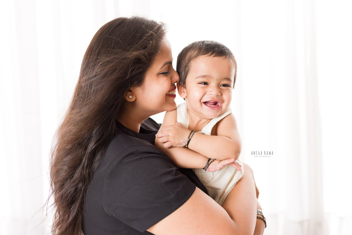 1-year-old boy posing with mom in a cute pose against a white backdrop, captured by Anega Bawa Photography for a family photoshoot in Gurgaon (Delhi NCR).