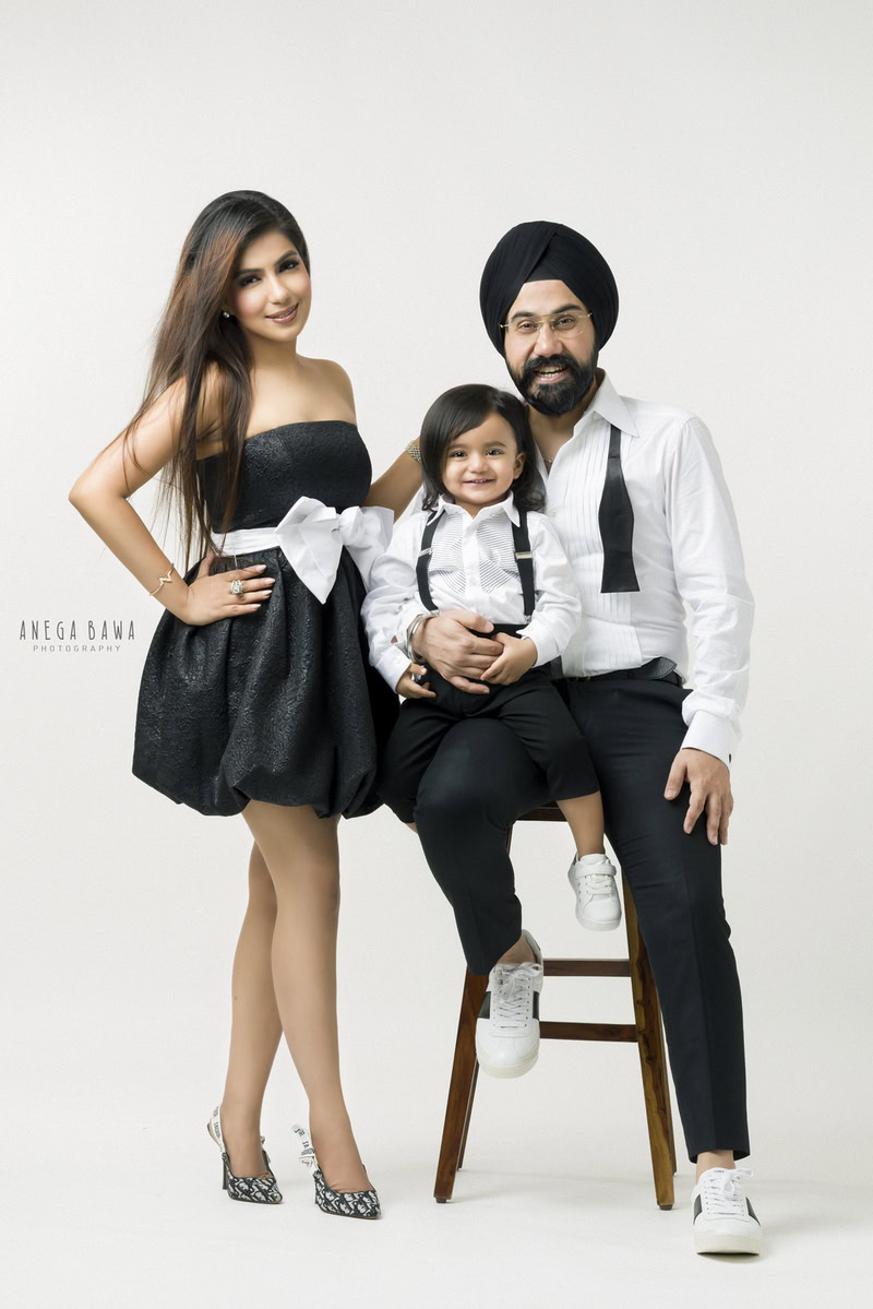 1-year-old boy seated on dad's lap with mom posing in front of a white backdrop, family photoshoot in Gurgaon (Delhi NCR)
