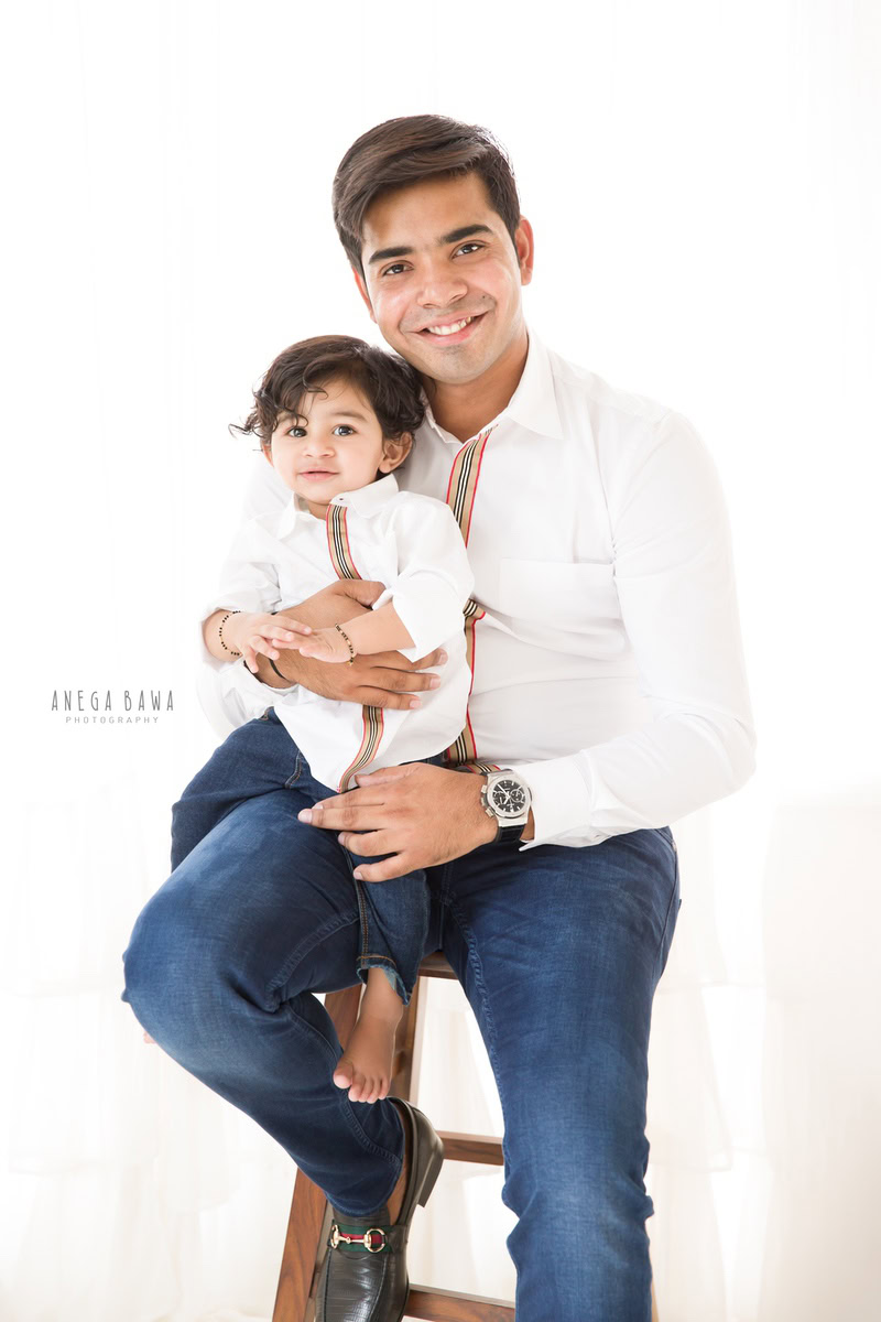 1-year-old boy seating on dad's lap against a white backdrop, captured by Anega Bawa, family photographer in Gurgaon (Delhi NCR).
