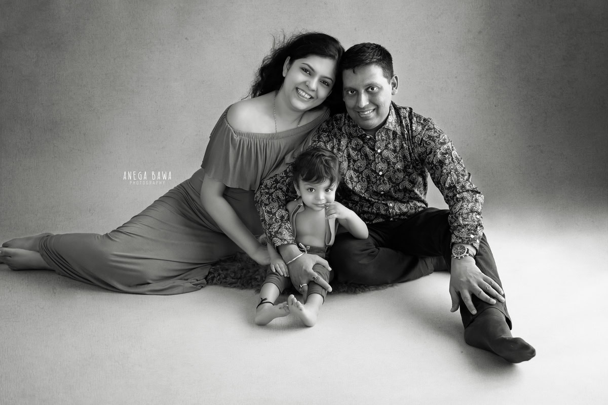 1-year-old boy seated on the floor with mom and dad against a black and white backdrop, captured by Anega Bawa Family Photographer Gurgaon (Delhi NCR).