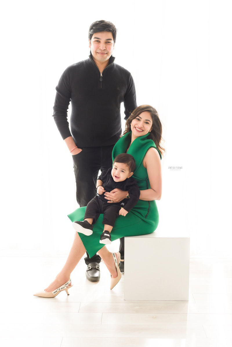 1-year-old boy seating on mom's lap with dad posing against a white backdrop, captured by Anega Bawa, family photographer in Gurgaon (Delhi NCR).