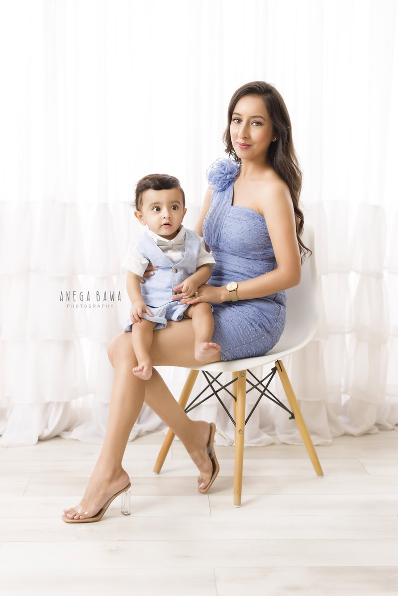 1-year-boy seated on mom's lap against a serene white backdrop, beautifully captured by Anega Bawa Photography for a family photoshoot in Gurgaon (Delhi NCR).