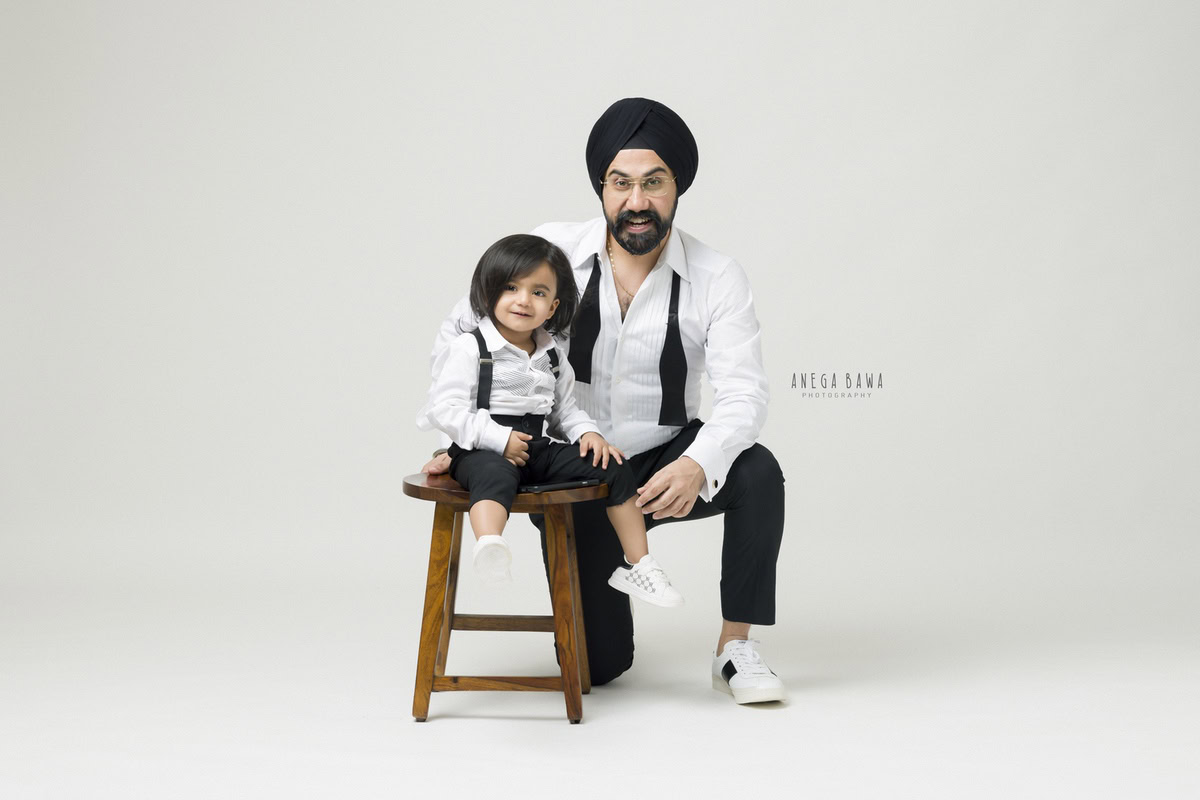 1-year-old boy seated on a stool, posing with dad against a white backdrop, captured by Anega Bawa Family Photographer Gurgaon (Delhi NCR).
