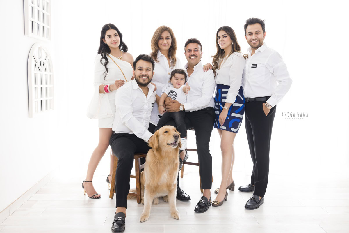 1-year-old boy seating on uncle's lap, posing with the family dog against a white backdrop, captured by Anega Bawa, family photographer in Gurgaon (Delhi NCR).