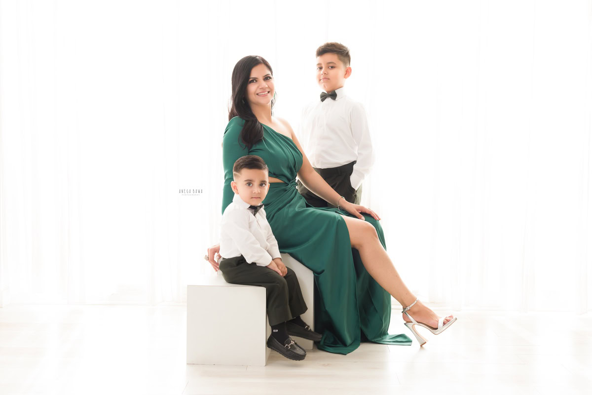 1-year-boy-seating-on-white-stool-posing-with-mom-elder-brother-white-backdrop