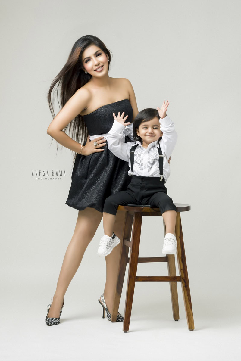 Charming 1-year-old boy seated on a rustic wooden stool, posing with his loving mom against a serene white backdrop, captured by Anega Bawa Family Photographer Gurgaon (Delhi NCR).