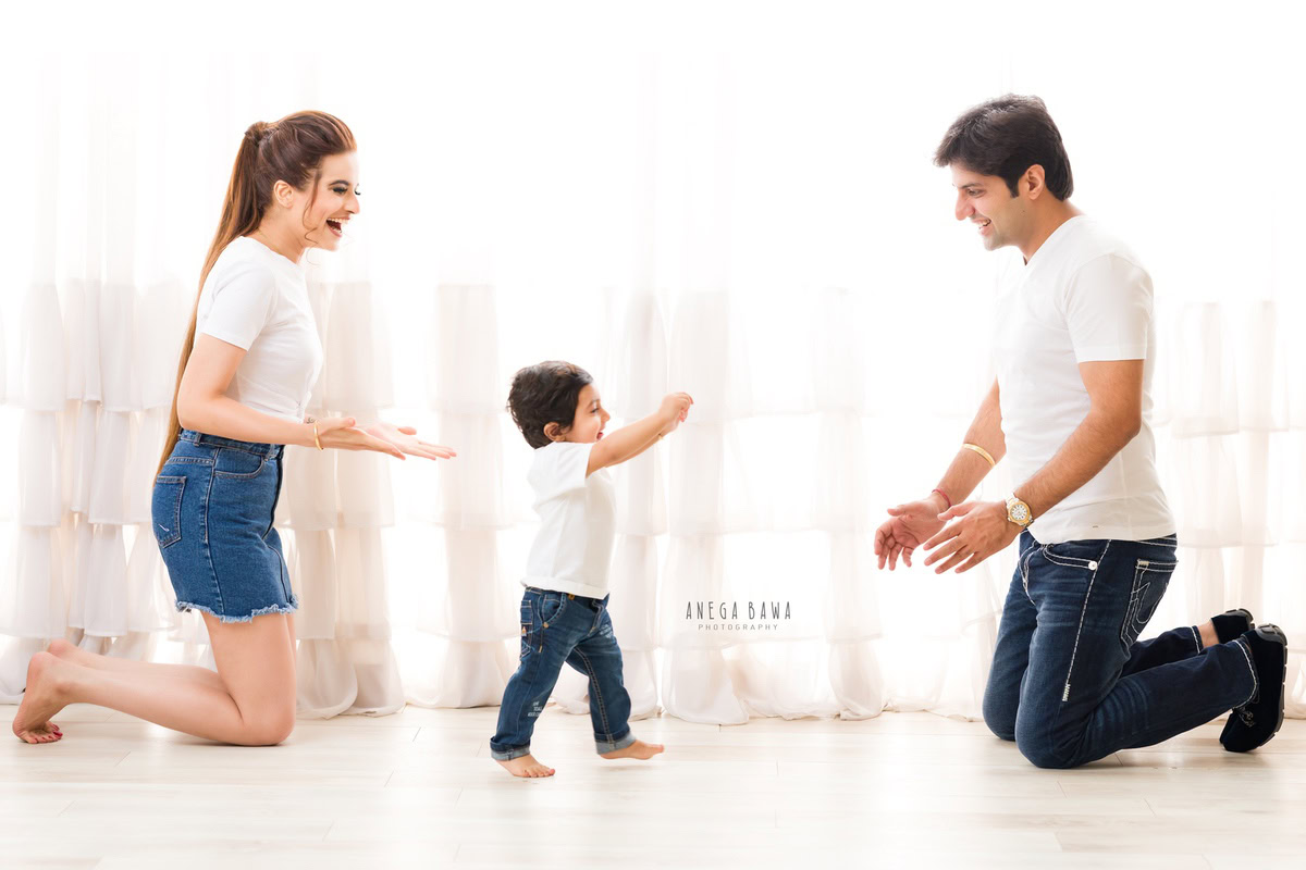 1-year-old boy standing on the floor, joyfully playing with his mom and dad against a clean white backdrop.
