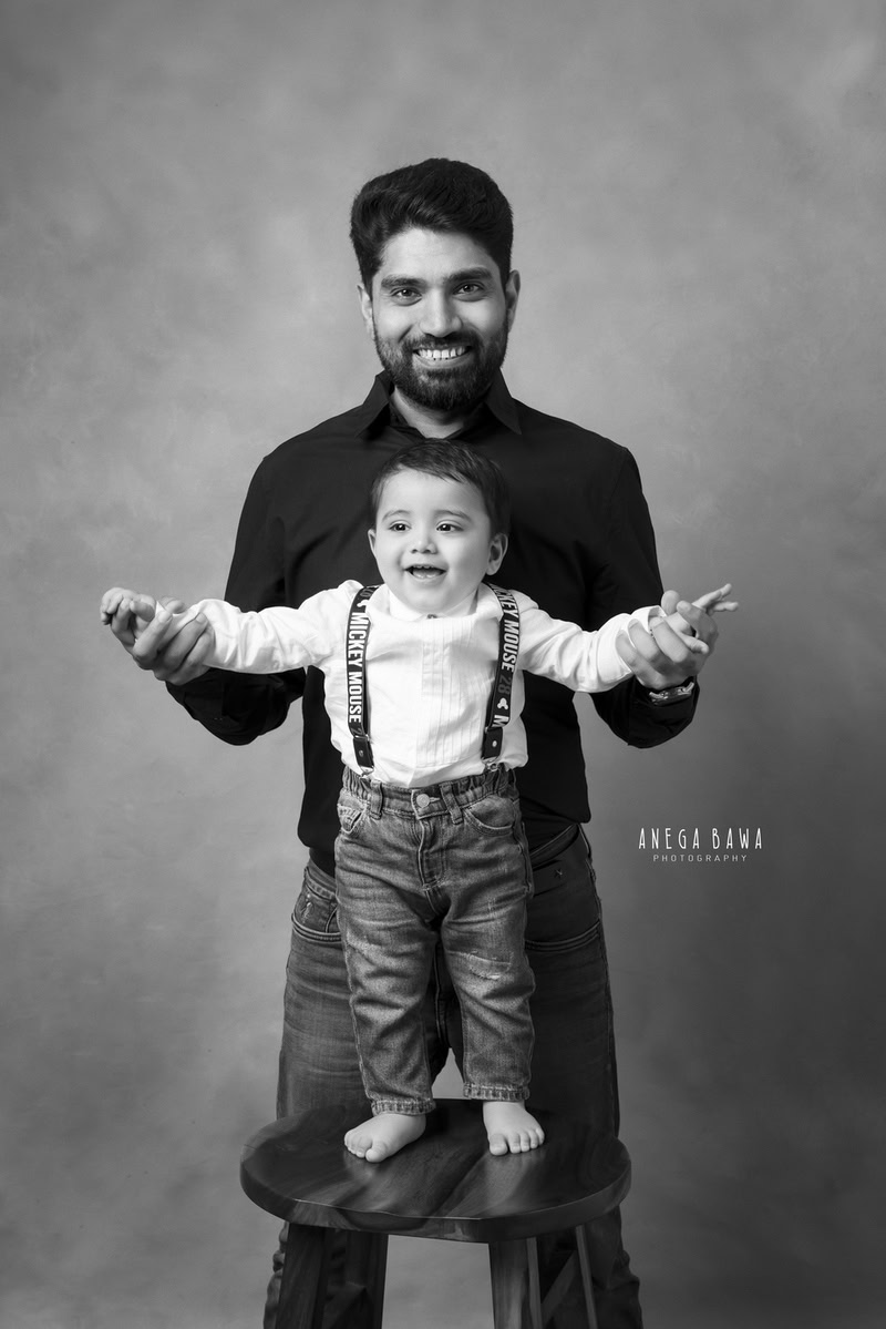 1-year-old boy standing on a wooden stool, posing with dad against a dull backdrop in a black and white pose