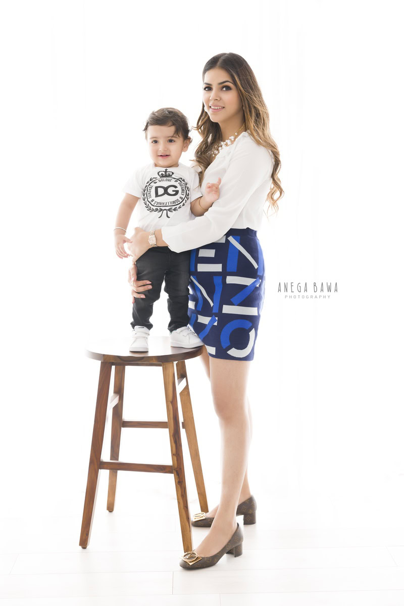 1-year-old boy standing on a wooden stool, posing with mom against a white backdrop, captured by Anega Bawa Family Photographer Gurgaon (Delhi NCR).