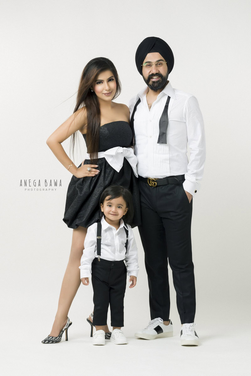 1-year-old boy standing with mom and dad, dressed in black and white, against a white backdrop, captured by Anega Bawa Photography for a family photoshoot in Gurgaon (Delhi NCR).
