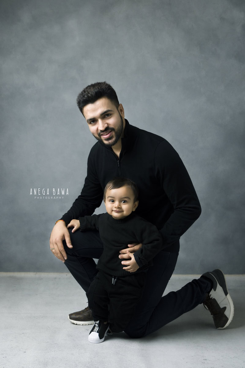 1-year-old boy twinning with dad, both wearing black, against a grey backdrop, photography done by Anega Bawa, Gurgaon (Delhi, NCR)
