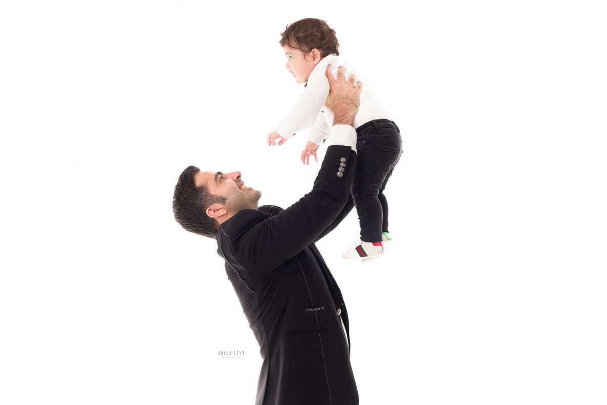 -year-old boy in white shirt, lifted in dad's arms, striking a cute pose against a white backdrop