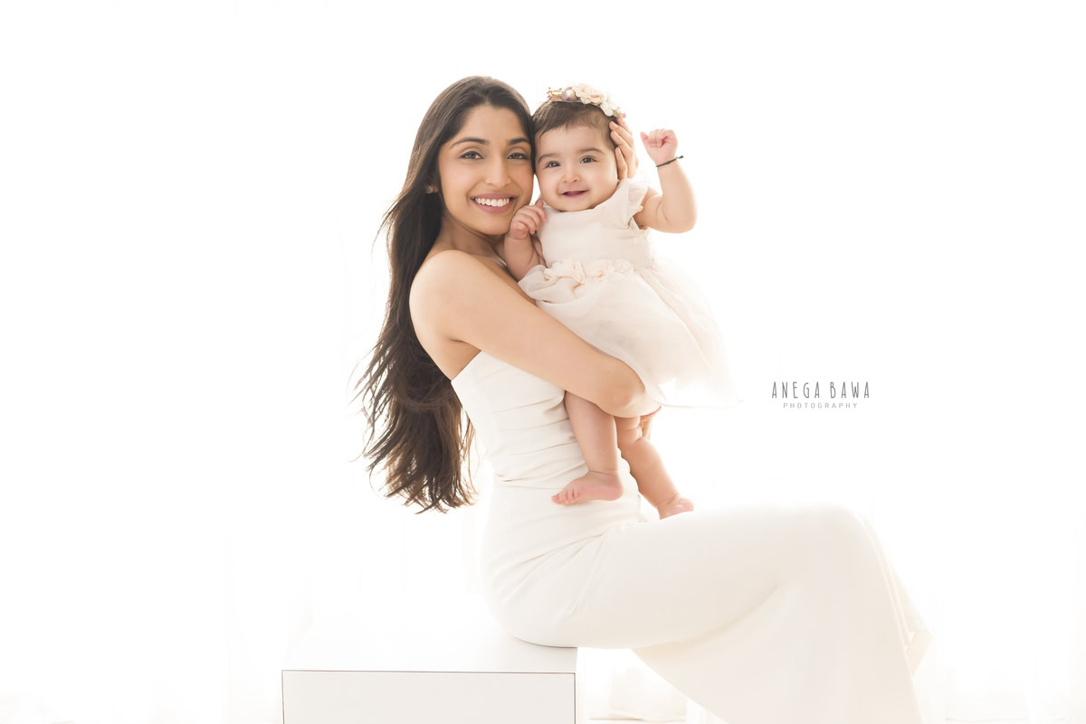 1-year cute girl posing with mom in a laughing pose against a white backdrop, captured by Anega Bawa Photography for a family photoshoot in Gurgaon (Delhi NCR).