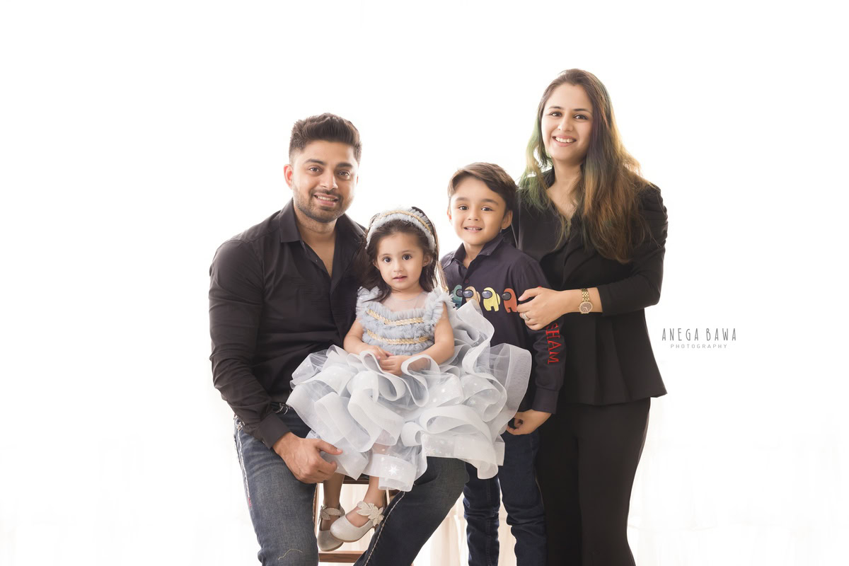 1-year-old girl in a fairy dress joyfully posing with her elder brother, mom, and dad in a heartwarming family portrait against a serene white backdrop. Captured by Anega Bawa Photography, ensuring memorable family moments in Gurgaon (Delhi NCR).
