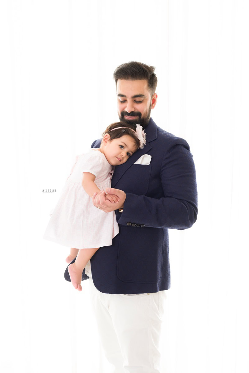 1-year girl hugging dad, posing cutely in front of a white backdrop.