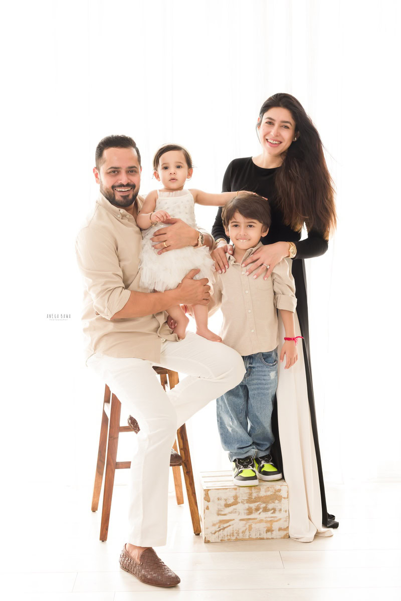 1-year-old girl, cradled in dad's arms, poses with mom and elder brother in a family portrait against a serene white backdrop, beautifully captured by Anega Bawa Photography in Gurgaon (Delhi NCR).