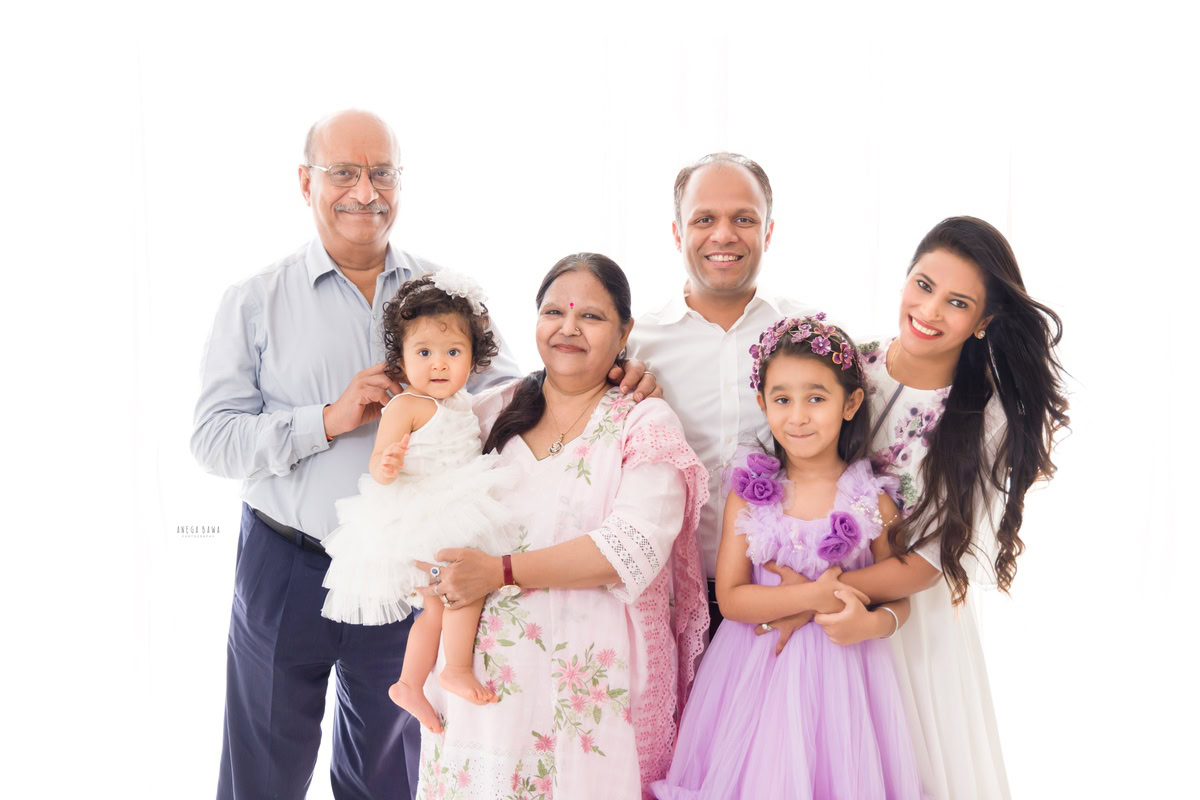 1-year-old girl in granny's arms, with elder sister, mom, dad, and grandfather in a family pose against a white backdrop, family photoshoot by Anega Bawa, Gurgaon (Delhi, NCR)