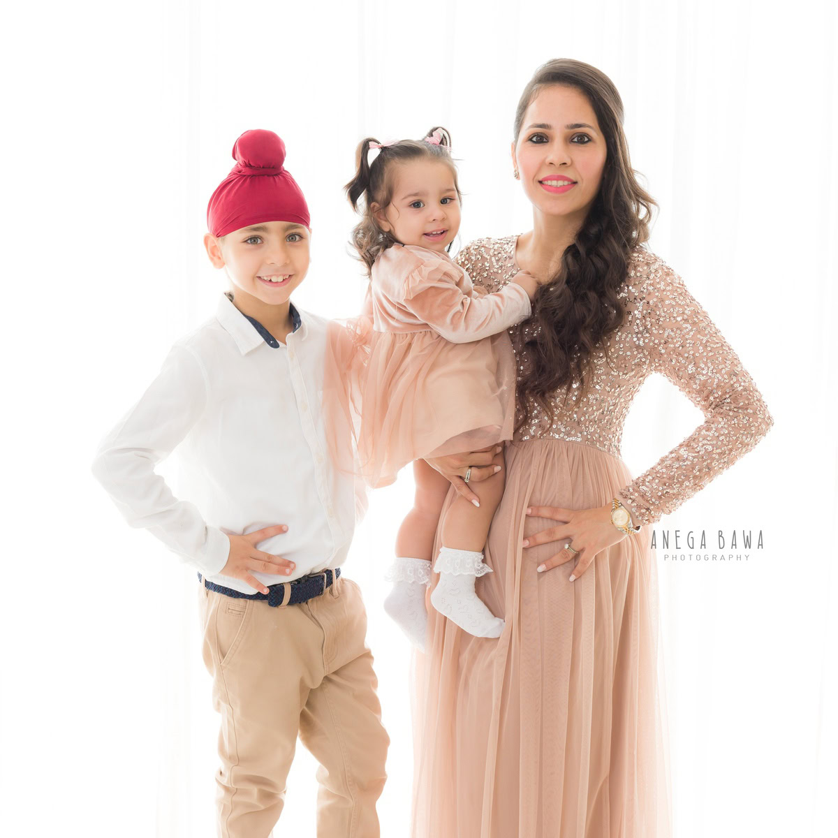 1-year-old girl in mom's arms, accompanied by her elder brother, against a clean white backdrop, captured beautifully by Anega Bawa in Gurgaon (Delhi, NCR).