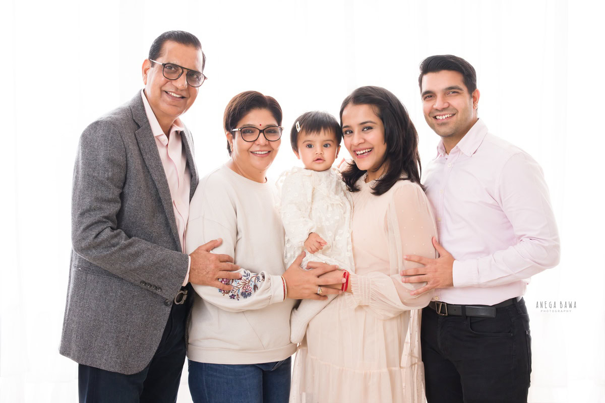 1-year-old girl in mom's arms, posing with dad and grandparents against a white backdrop, family photoshoot by Anega Bawa, Gurgaon (Delhi, NCR)