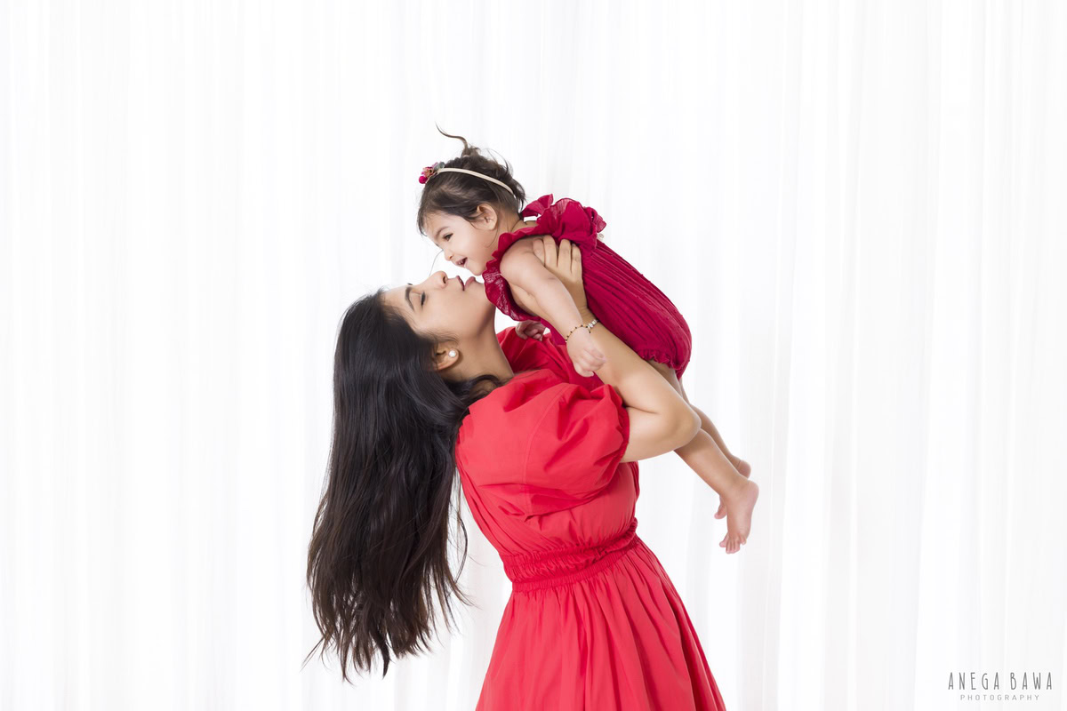 1-year-old girl held lovingly in her mom's arms against a clean white backdrop, captured by Anega Bawa Photography for a family photoshoot in Gurgaon (Delhi NCR).