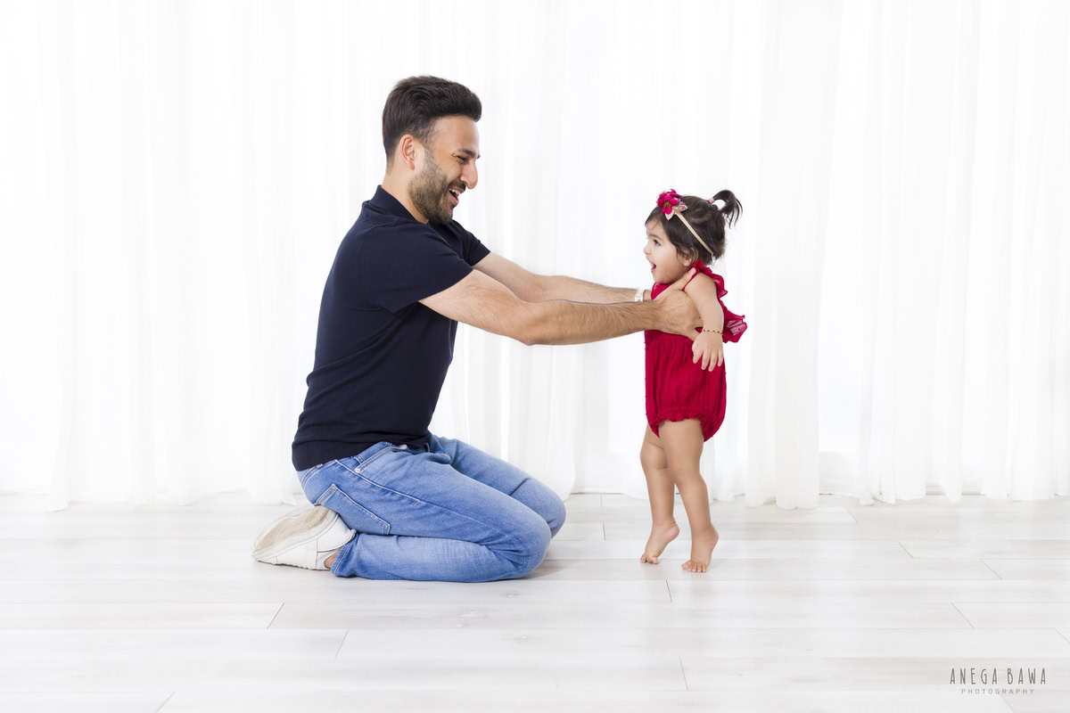 1-year-old girl playing gleefully with dad on a pristine white backdrop, captured beautifully by Anega Bawa Photography for a family photoshoot in Gurgaon, Delhi NCR.