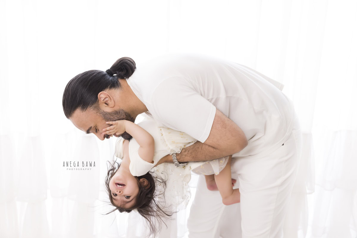 1-year-old girl playing with dad, both twinning in white, against a white backdrop, family photoshoot by Anega Bawa, Gurgaon (Delhi, NCR)