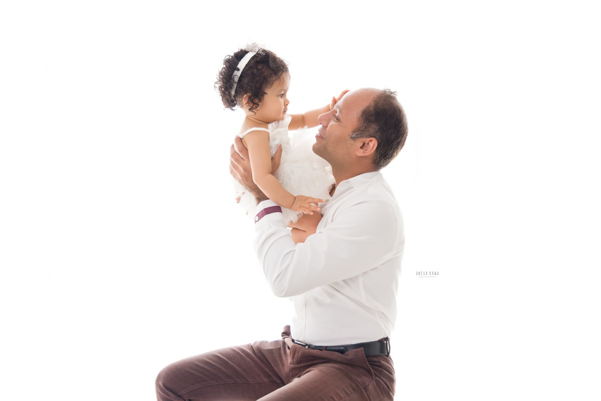 1-year-old girl joyfully playing with dad against a crisp white backdrop, captured by Anega Bawa Photography in Gurgaon (Delhi NCR).