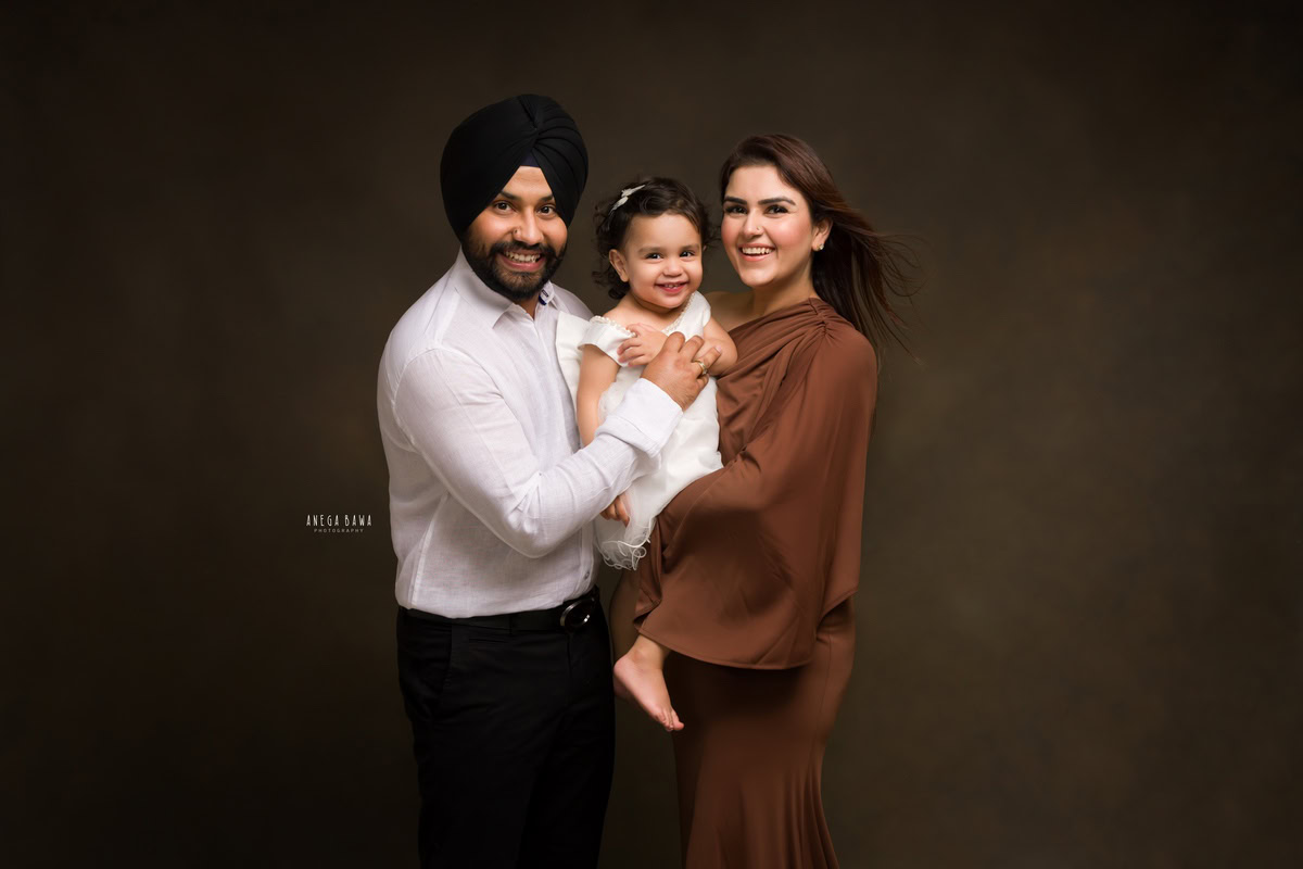 1-year-old girl poses with mom and dad against a brown backdrop, family photoshoot by Anega Bawa, Gurgaon (Delhi, NCR)