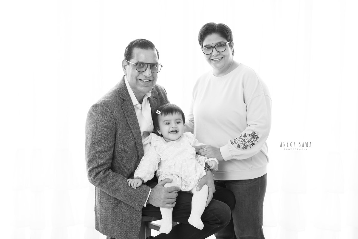 1-year-old girl posing cutely with grandparents against a white backdrop, family photoshoot by Anega Bawa, Gurgaon (Delhi, NCR)