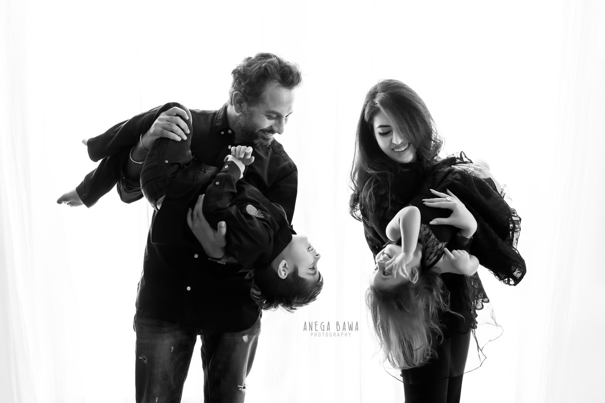 1-year-old girl posing cutely with mom, dad, and elder brother in a family pose against a white backdrop, family photoshoot by Anega Bawa, Gurgaon (Delhi, NCR)