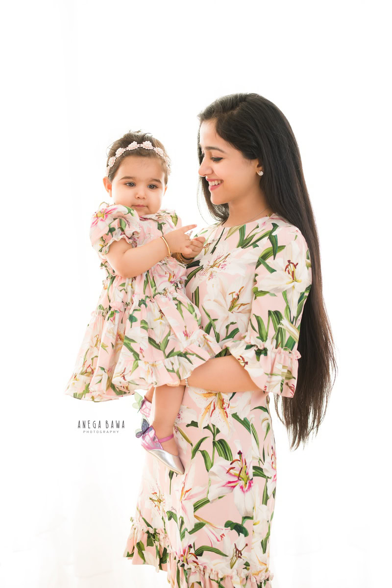 1-year-old girl posing cutely with mom, both twinning in floral dresses, against a white backdrop, captured by Anega Bawa, family photographer in Gurgaon (Delhi NCR).