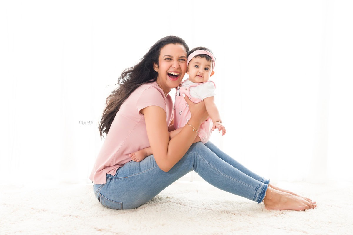 1-year-old girl posing cutely with mom, both twinning in floral dresses, against a white backdrop, captured by Anega Bawa, family photographer in Gurgaon (Delhi NCR).