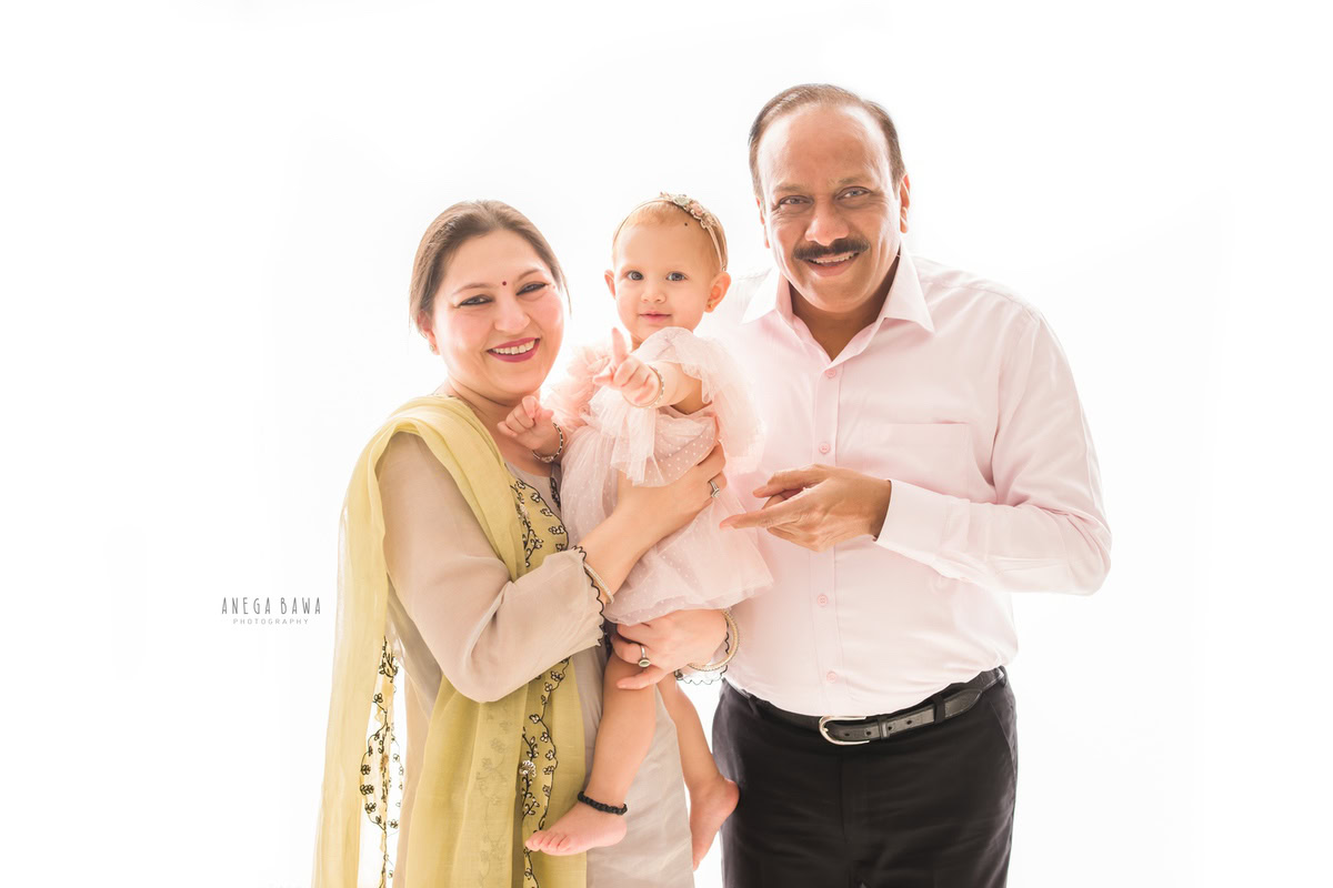 1-year-old girl posing with her grandparents against a white backdrop, captured by Anega Bawa Family Photographer Gurgaon (Delhi NCR).