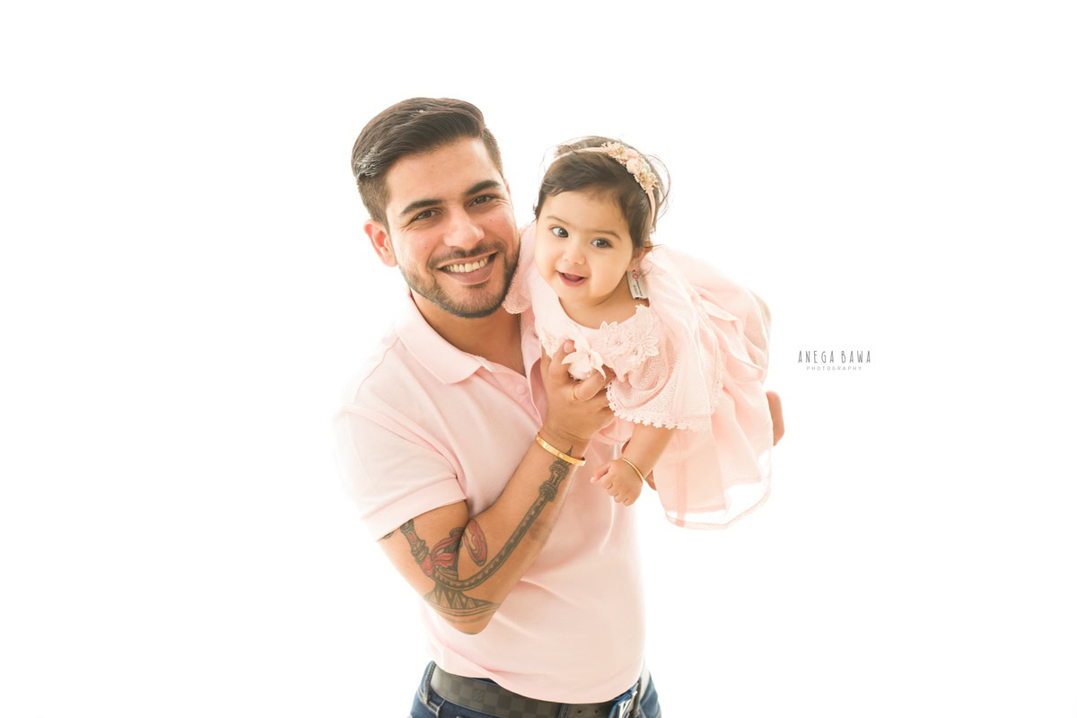 1-year girl posing with dad in a cute headband against a serene white backdrop, captured by Anega Bawa Photography in Gurgaon (Delhi NCR).
