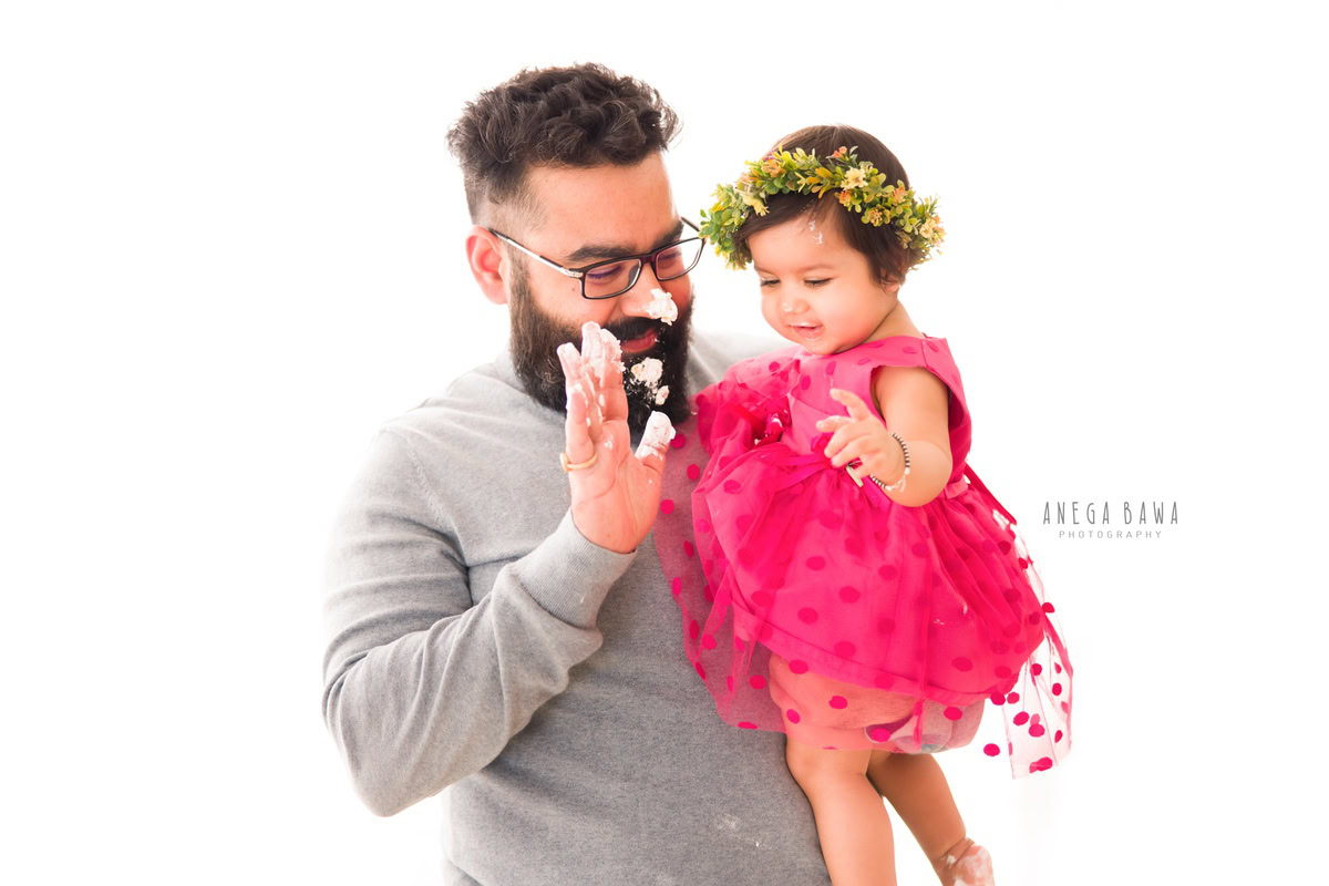 1-year-old girl posing with dad in a cute pink dress and tiara band against a white backdrop, captured by Anega Bawa Family Photographer Gurgaon (Delhi NCR).