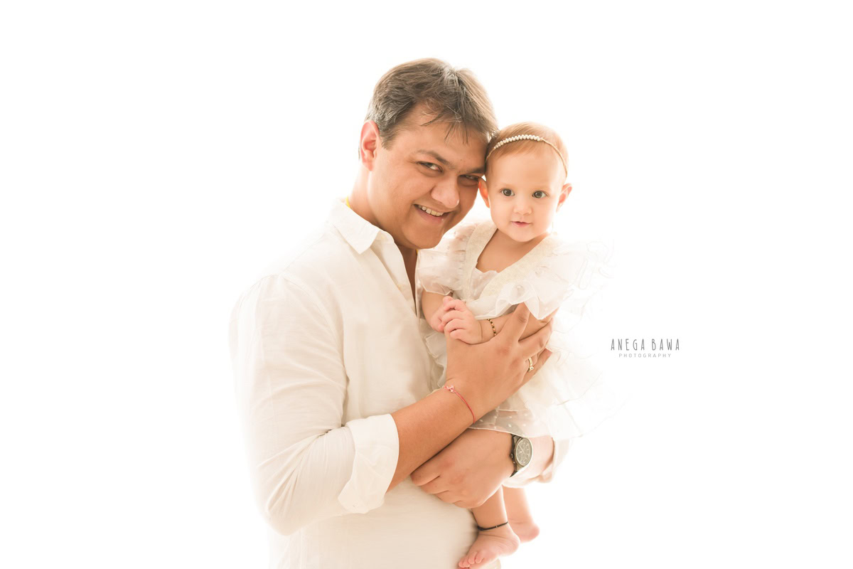 1-year-old girl posing with dad in a cute, smiling pose against a white backdrop, captured by Anega Bawa Family Photographer Gurgaon (Delhi NCR).