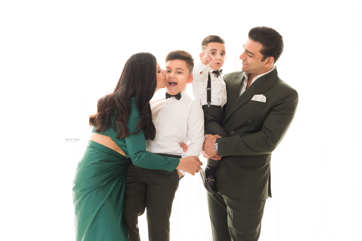 1-year-old girl posing with dad, mom, and elder brother against a white backdrop, captured by Anega Bawa, family photographer in Gurgaon (Delhi NCR).